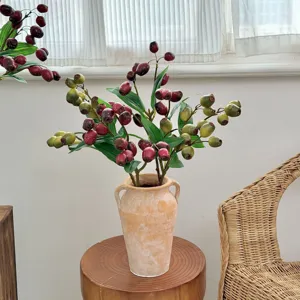 Detailed view of realistic artificial berry branches in a rustic wabi-sabi clay vase.