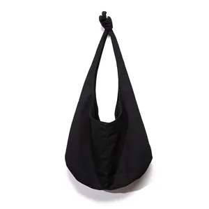 Vista frontal del bolso de lona negro con detalle de nudo colgado en una pared blanca.