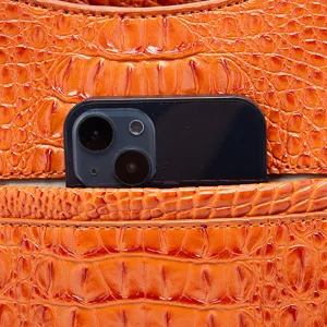 Primer plano de bolso naranja con relieve de cocodrilo y teléfono en el bolsillo.
