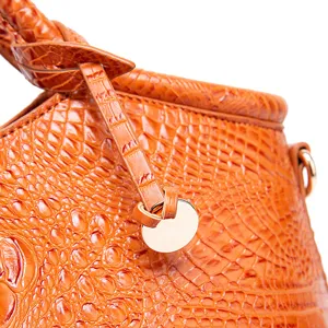 Detalle macro de la textura de cocodrilo naranja y herrajes dorados en el bolso de cuero.