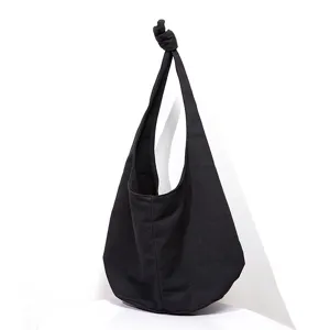 Vista de detalle de un bolso hobo de lona negra con una elegante correa anudada