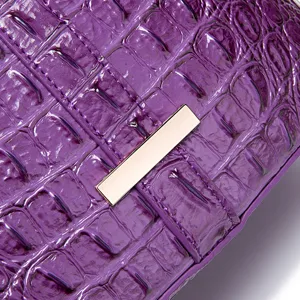 Primer plano de cuero grabado de cocodrilo púrpura con herrajes dorados elegantes.