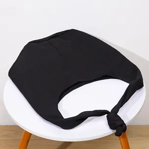 Vista detallada de un bolso de lona negro con correa anudada sobre una mesa blanca mínima