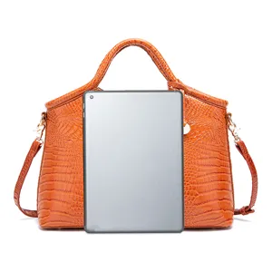 Detalle que muestra el tamaño del bolso naranja con relieve de cocodrilo frente a una tablet.