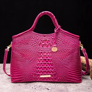 Vista detallada de un bolso magenta con textura de cocodrilo, herrajes dorados y correa