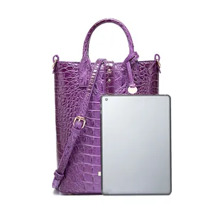 Vista detallada del bolso morado con relieve de cocodrilo y tableta para comparación