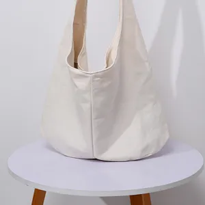 Detalle de un bolso hobo minimalista de lona de algodón crema sobre una mesa blanca.