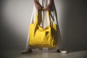 Bolso tote grande de cuero suave amarillo vibrante con bolsillo frontal sostenido.