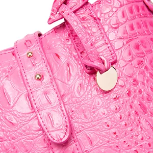 Detalle de cerca de un bolso rosa con textura de cocodrilo en relieve y tachuelas doradas.