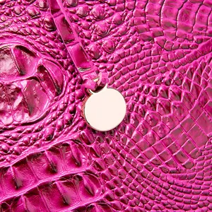 Detalle de la textura de piel de cocodrilo grabada en magenta con un dije metálico