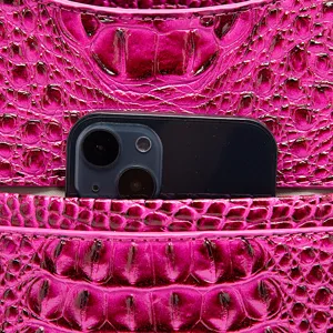 Detalle macro de bolso rosa con relieve de cocodrilo y smartphone en el bolsillo