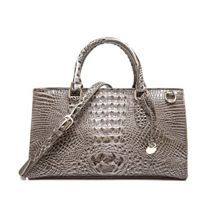 Detalle de bolso de mano gris con grabado de cocodrilo y herrajes dorados elegantes.