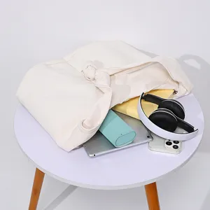 Vista de detalle del bolso de lona crema en mesa con electrónica y libros de estilo