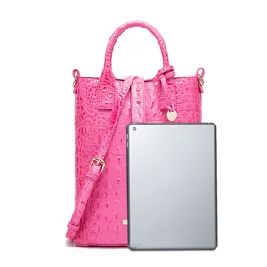 Bolso rosa con grabado de cocodrilo mostrado con una tableta para comparar tamaño