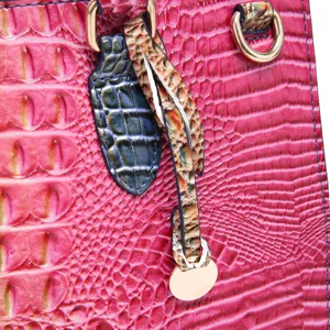 Detalle de bolso fucsia con relieve de cocodrilo y herrajes dorados en primer plano.