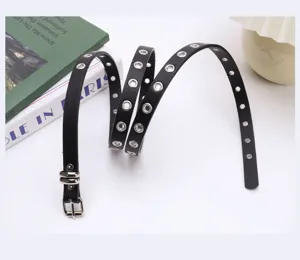 Close-up detail of black punk leather belt with silver grommet holes and buckle