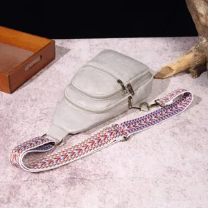 Detalle de bolso bandolera gris con correa boho tejida y herrajes de bronce clásicos
