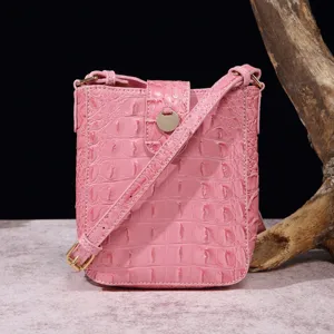 Detalle de un elegante bolso bandolera rosa con textura de cocodrilo y herrajes dorados