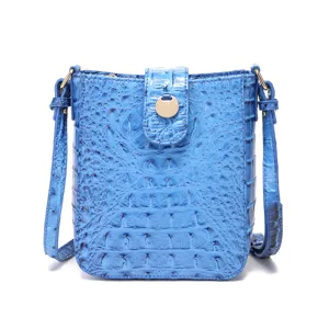 Detalle de bolso bandolera azul con relieve de cocodrilo y broche redondo dorado