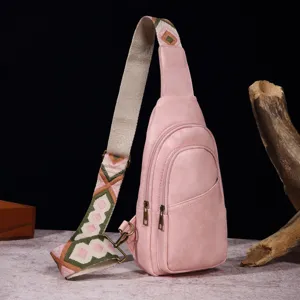 Detalle de un bolso bandolera rosa de cuero sintético con correa de estilo bohemio.