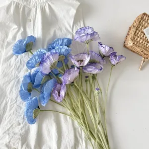 Detalle de amapolas artificiales azules y moradas sobre una camisa blanca