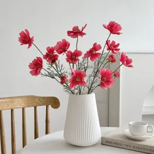 A detailed macro view of vibrant pink artificial cosmos flowers in a white ribbed vase.