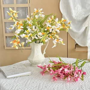 Detailed view of artificial orchid flowers in white vase and on tablecloth