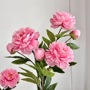 Close-up of realistic pink artificial peonies with lush petals and green leaves.