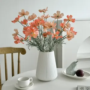 Macro view of artificial orange cosmos flowers in a white fluted ceramic vase on a table.