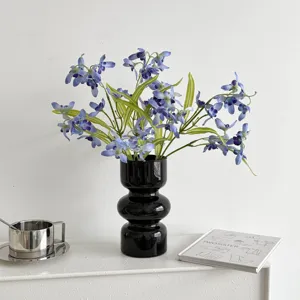Detail shot of blue artificial flowers in a modern black vase on a white shelf.