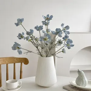 Realistic blue artificial cosmos flowers arranged in a minimalist white ribbed ceramic vase