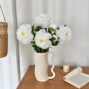 Close-up of elegant white artificial peony flowers inside a wavy cream ceramic vase