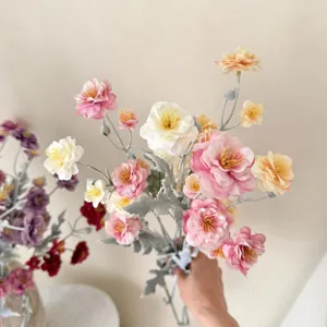Close-up detail of a hand holding a multi-head flocked artificial camellia flower bouquet.