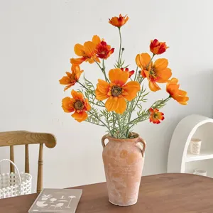 Close-up detail of vibrant orange artificial cosmos flowers in a rustic terracotta vase for decor