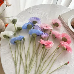 Vista detallada de amapolas artificiales de colores con tallos flocados sobre encaje