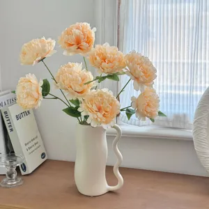 Realistic light orange artificial peony bouquet in a stylish white ceramic vase.
