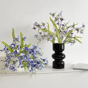 Detailed view of artificial blue and purple cymbidium orchids in a modern black vase.