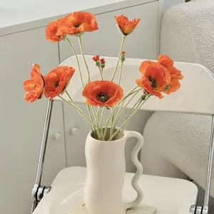 Detalle de amapolas artificiales naranjas con tallos flocados en un jarrón.