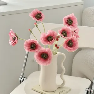 Detalle de amapolas artificiales rosas en un jarrón de cerámica ondulado minimalista