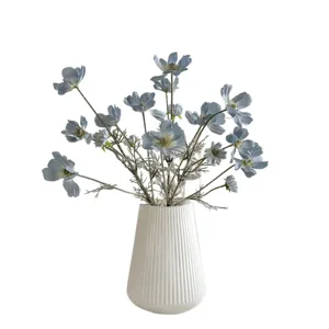 Elegant light blue artificial cosmos daisy flowers in a white ribbed ceramic vase