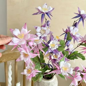Close-up of realistic pink and purple artificial Aquilegia flowers displayed in a ceramic vase