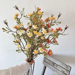 Autumn-toned artificial wild daisy bouquet held against a rustic white wall background.