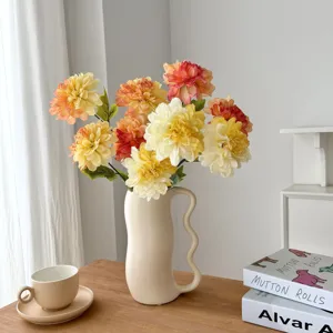 Artificial dahlia flower arrangement in a decorative cream wavy vase on a table