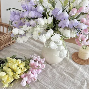Nahaufnahme von bunten künstlichen Maiglöckchen in einer eleganten weißen Keramikvase