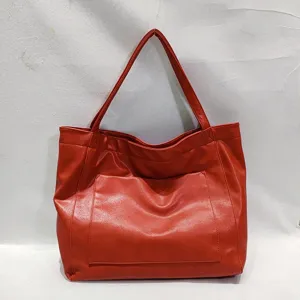 Detalle de bolso tote de cuero rojo encerado con bolsillo frontal y gran capacidad.