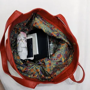 Vista detallada del interior de un gran bolso tote de cuero rojo con forro floral