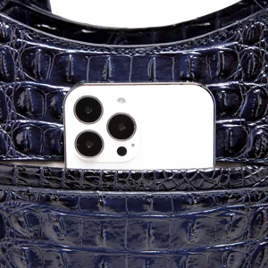 Primer plano de bolso con relieve de cocodrilo azul oscuro y móvil para referencia.