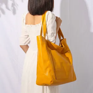 Vista detallata de un gran bolso tote amarillo de cuero encerado llevado al hombro por modelo