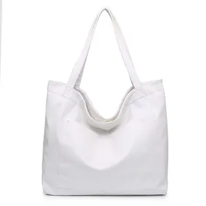 Vista frontal detallada de un bolso tote grande de cuero suave blanco con bolsillo frontal