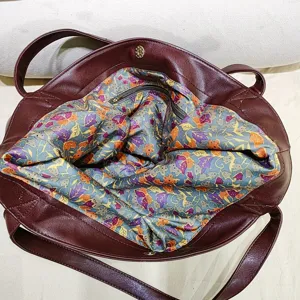 Detalle de bolso tote grande burdeos en cuero vintage con forro floral y bolsillo.